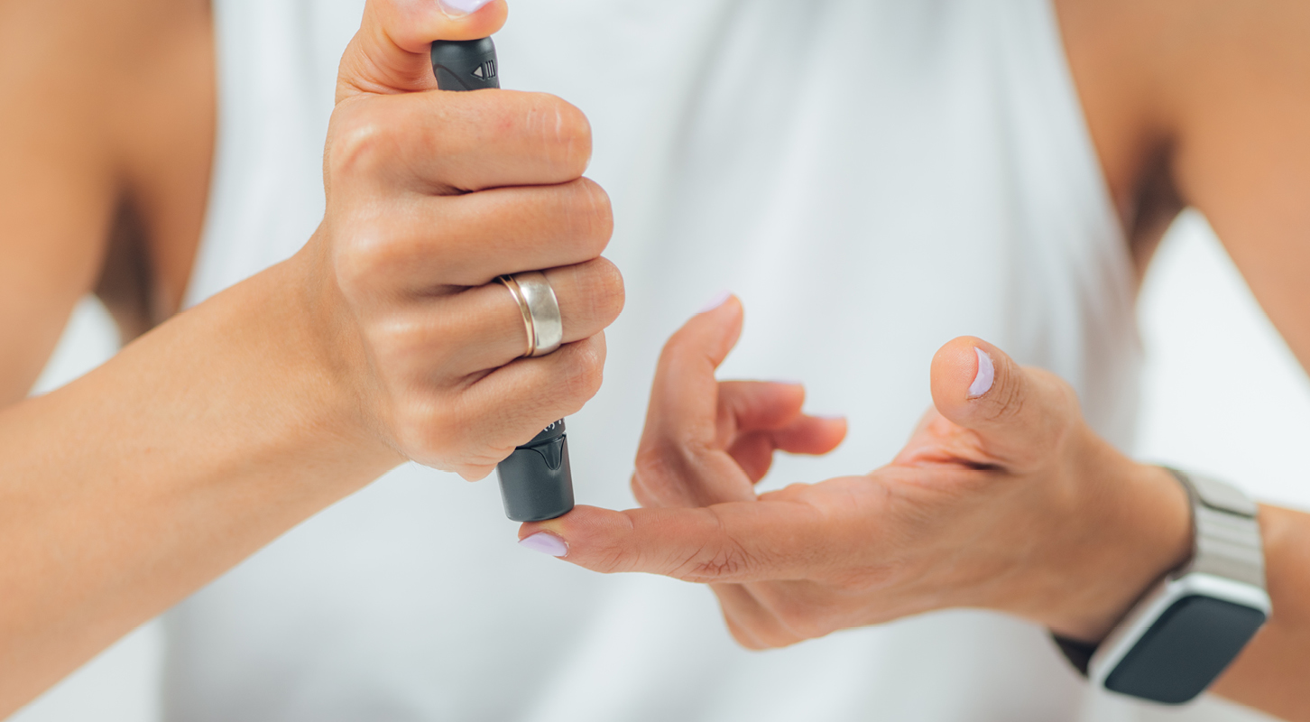 Woman pricking her finger with a blue lancing device to check her blood glucose 