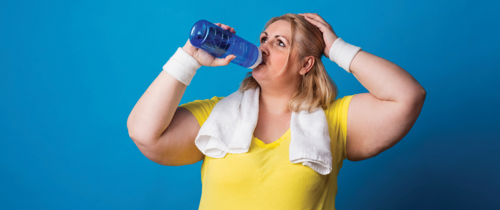 Heavy-set young woman in yellow shirt drinking water after exercising