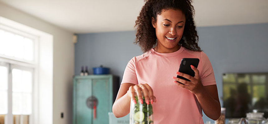 Young woman making smoothie after exercise and tracking calories on smart phone